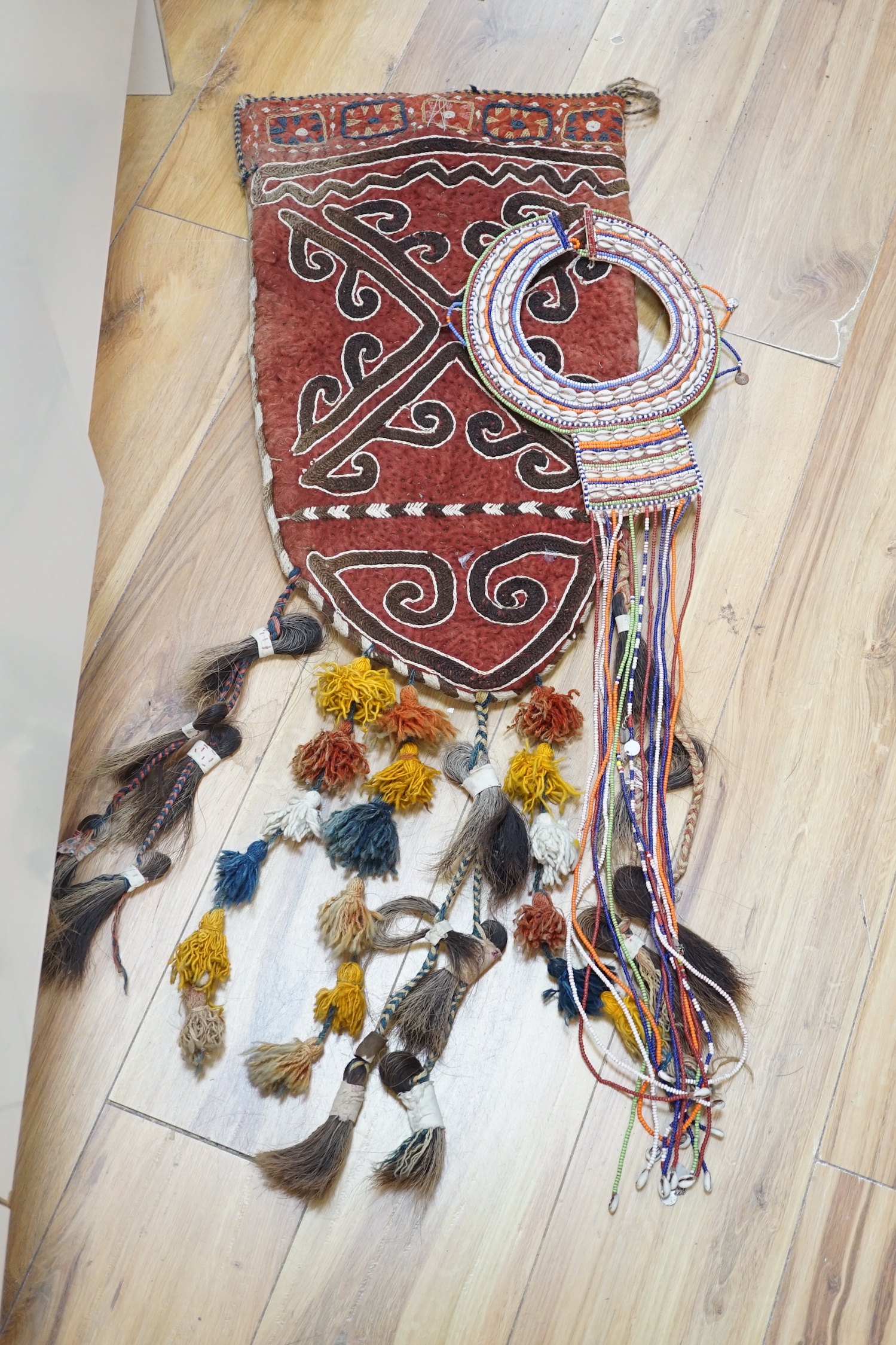 An African tribal bead and shell work necklace together with an embroidered Uzbek saddle bag with tassels and a similar felt wall hanging, the largest 110cm x 82cm